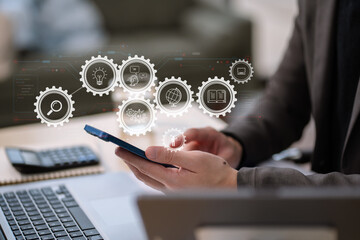 Businessman using smartphone and laptop with virtual network icons in office.