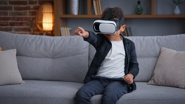 African American child boy kid son playing VR game at home play online 3d gaming with virtual reality glasses augmented headset AR technology gaming playing metaverse pretending fighting innovation