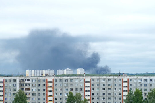 Black smoke billows on background over panel apartment buildings in modern city. Fire in the distance, catastrophe, dangerous fumes rising into the air. Cityscape in usual life with force majeure.