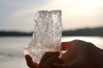 Man hand holding ice block on frozen river background at sunset in camping. Quiet peaceful place for rest relaxation on nature. Tourism, camping, outdoor recreation activity in cold season on weekend.