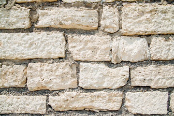 Textured wall of rectangular stone blocks in light beige shades and cement between them.