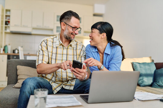 Young couple checking bills and calculating expenses using a laptop at home, debt taxes concept, worried married elderly couple