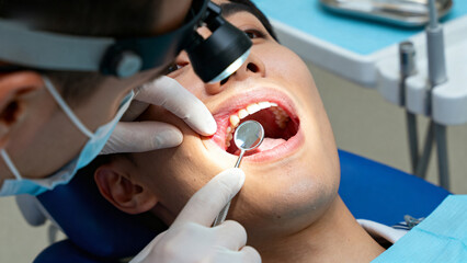 Dentist examining a patient's teeth using a dental mirror and light in a clinical setting