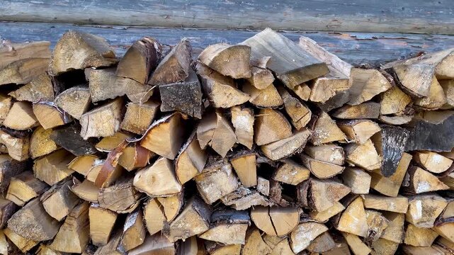 Stack of firewood piled against the wall of a wooden rural house, used as fuel for a traditional household stove.

