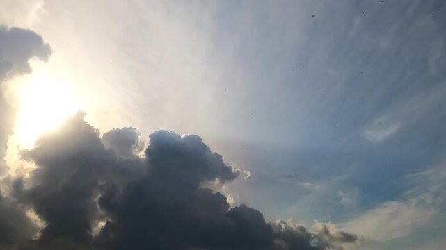 Cumulus and stratus clouds quickly changing shapes in the wind. Low angle view at the sky with transforming cloudscape covering the sun. Timelapse.