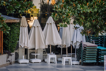 Closed sun umbrellas and stacked lounge chairs are neatly arranged on a tiled patio, likely at a resort or pool area during off-hours or end of the day.