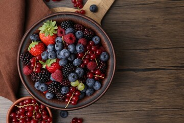 Different ripe berries in bowls on wooden table, flat lay. Space for text