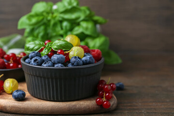Different ripe juicy berries and basil in bowl on wooden table, closeup. Space for text