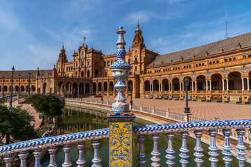 Obraz premium a close-up of a beautifully decorated blue and white ceramic balustrade at the Plaza Spain in Seville, with the plaza's intricate Renaissance architecture and a reflective canal in the background