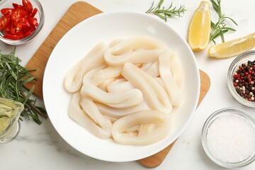 Uncooked squid rings and spices on white table, flat lay