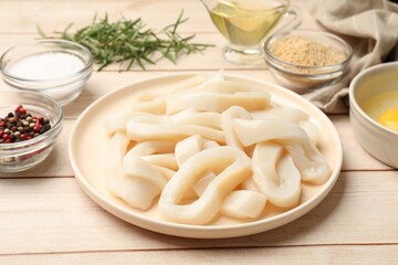 Uncooked squid rings, spices, yolk and bread crumbs on wooden table, closeup