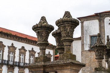 a close-up view of intricately carved stone balustrades with a background of a classic building featuring a door and windows with blue shutters. The architectural elements weathered, indicating age