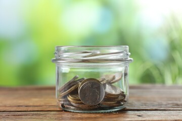 Glass jar with coins on wooden table against blurred background, closeup