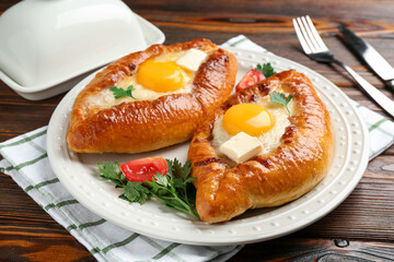 Tasty khachapuri with cheese and eggs served on wooden table, closeup