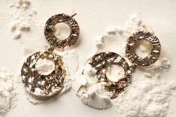 Stylish gold earrings on sand, top view