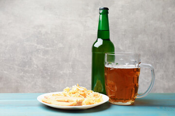 Dried squid snacks and beer on light blue wooden table against grey background, closeup