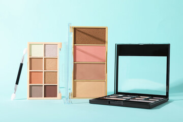Colorful eyeshadow palettes and applicator on turquoise background, closeup