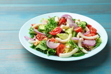Delicious salad with squid, vegetables and walnuts on light blue wooden table, closeup