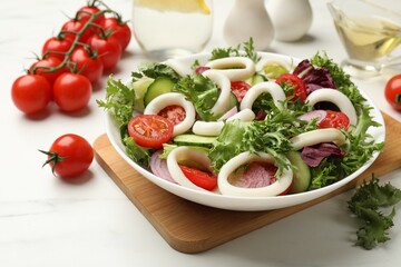 Delicious salad with squid rings and vegetables on white marble table, closeup