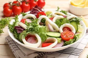 Delicious salad with squid rings and vegetables on light wooden table, closeup
