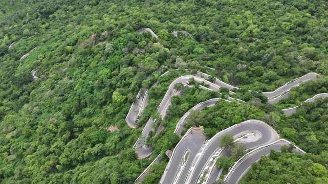 Kolli Malai, Tamil Nadu. The thrilling 70 hairpin bends are seen ascending a lush, green mountain under a bright sky. Captures the iconic road infrastructure.