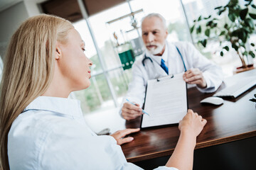Fototapeta premium Doctor Consults Patient in Office Environment Discussing Healthcare Paperwork and Medical Treatment Options