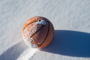 Basketball partially covered in snow on a bright winter day, symbolizing off-season sports, outdoor...
