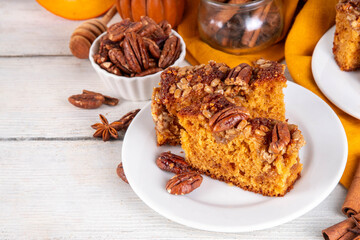Autumn sweet dessert pumpkin bread cake with caramel, maple syrup or honey, sunflower seeds, and pecan nuts on white wooden background with ingredient for baking, copy space