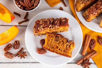 Autumn sweet dessert pumpkin bread cake with caramel, maple syrup or honey, sunflower seeds, and pecan nuts on white wooden background with ingredient for baking, copy space