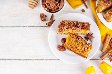 Autumn sweet dessert pumpkin bread cake with caramel, maple syrup or honey, sunflower seeds, and pecan nuts on white wooden background with ingredient for baking, copy space
