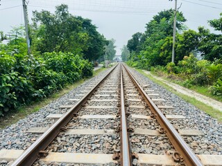 Obraz premium Railway line in the middle, green trees on both sides and blue sky above. 