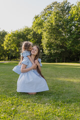 Daughter hugs and kisses her mother in the sunlight, wearing blue dresses. Close-up portrait of happiness. Family concept, interaction between parents and children © Татьяна Зернова