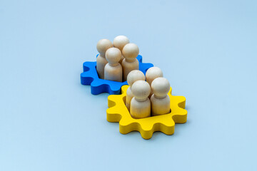Wooden human figures inside blue and yellow gear shapes. Mergers and acquisitions, teamwork,...