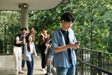 A group of university students standing together, gossiping and pointing playfully at a male...