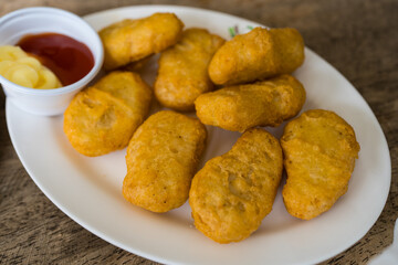 Golden crispy chicken nuggets piled together with ketchup on a white dish