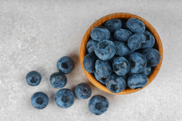 Fresh ripe blueberries in small wooden bowl on gray textured stone background. Delicious organic fruit rich in vitamins, wild berries,healthy lifestyle, natural food. Close up, macro, top view
