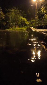 Atmospheric video of rainstorm in a night city.Heavy rain passing through puddles taken from low point. Large drops break on the pavement in the light of street lamps. Vertical screen
