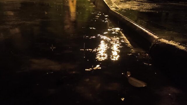 Atmospheric video of rainstorm in a night city.Heavy rain passing through puddles taken from low point. Large drops break on the pavement in the light of street lamps.	

