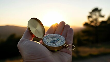 Man holding a vintage golden compass in his hand at sunset, symbolizing guidance and future direction for life path footage. - Powered by Adobe