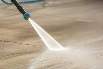 High pressure water hose cleaning outdoor patio surface, powerful spray removing dirt from concrete tiles in bright daylight