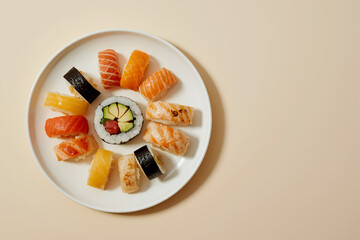 Assorted sushi ring on white plate with center maki; salmon, tuna, shrimp nigiri on beige background with wide clean copy space.