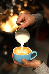 A barista makes a cappuccino with beautiful latte art against the backdrop of a coffee machine with bright background lighting.