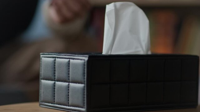 Close up shot of unrecognizable patient taking tissues from tissue box during therapy session with psychologist approaching and supporting him in emotional pain