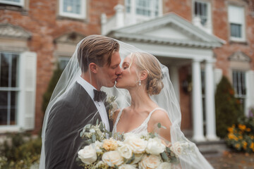 Photo of bride and groom kissing under a veil. Shot of newly married couple on the beach on their wedding day.