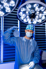 Plastic surgeon holding breast implant in operating room. Surgeon in mask and scrubs holds a...