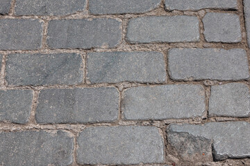 The old street is paved with paving stones. Background of dark stones laid on the road in an ancient city. Paving stones in an ancient city.