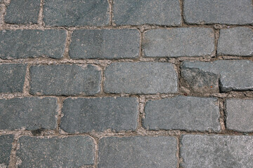 The old street is paved with paving stones. Background of dark stones laid on the road in an ancient city. Paving stones in an ancient city.