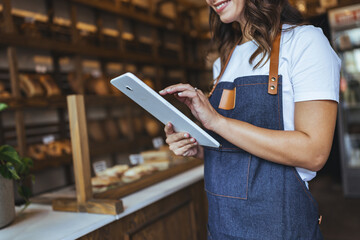 Smiling Woman In Denim Apron Using Tablet In Bakery Shop