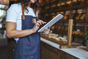 Bakery Worker in Denim Apron Using Tablet Behind Pastry Display for Stock Photo