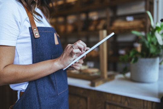 Baker in Denim Apron Using Tablet in Cozy Bakery Setting Demonstrating Modern Kitchen Management - Powered by Adobe